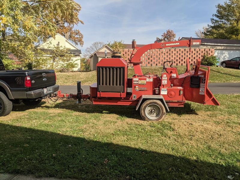 A red wood chipper hitched behind a pickup on a lawn.